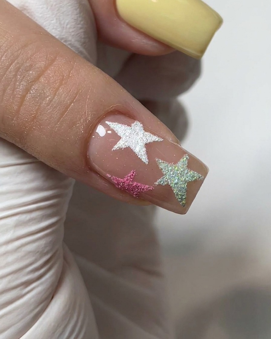 A brush applying a clear glossy top coat over a nail decorated with chrome powder and textured stars.