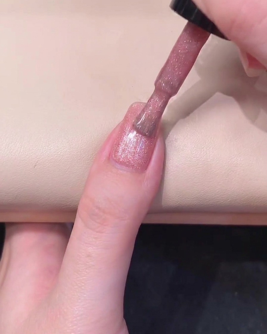A black cylindrical magnet held parallel to the right side of a pink gel-coated nail to activate shimmer.
