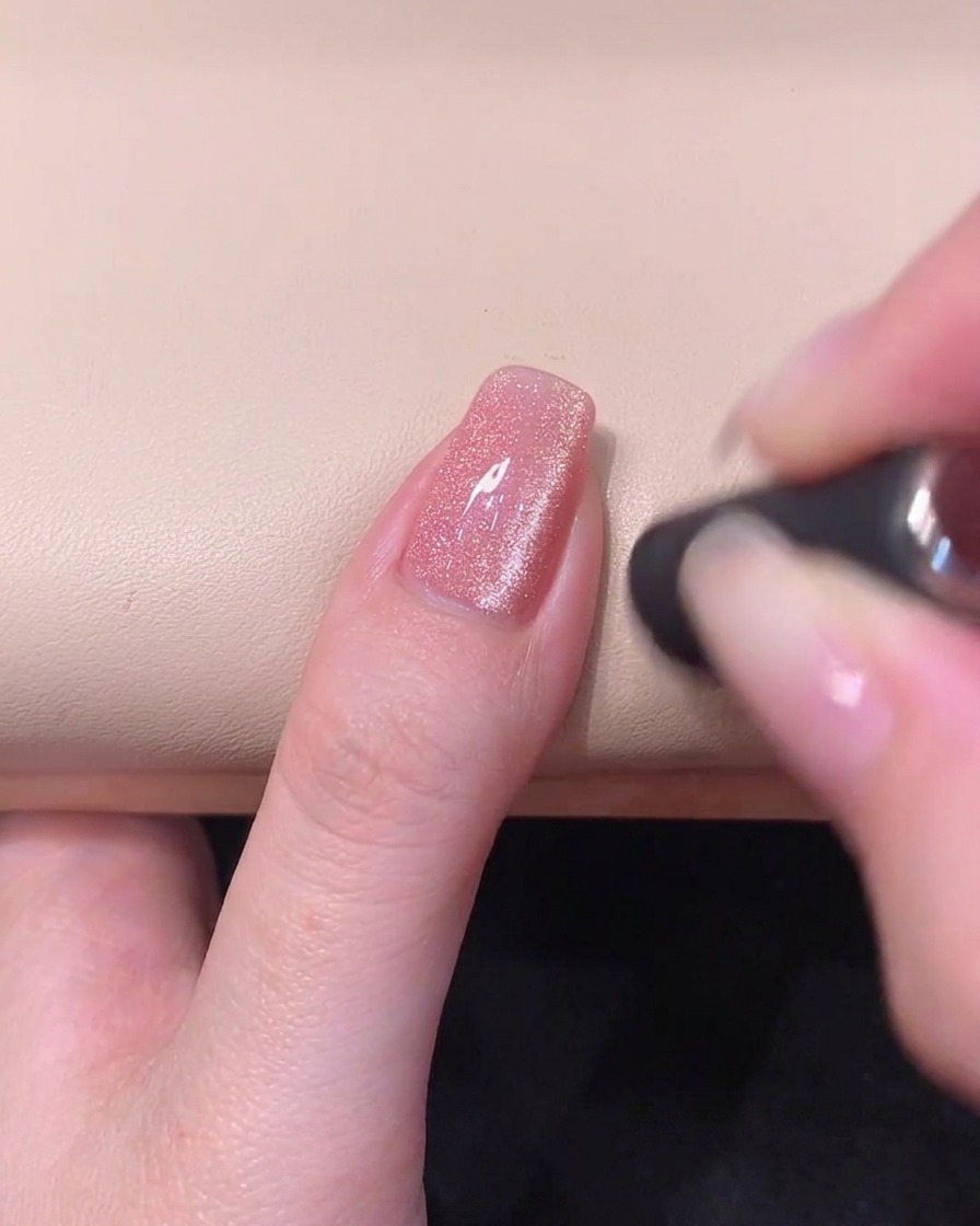 A cylindrical magnet held horizontally across the top free edge of the nail to form a bright cat-eye band.