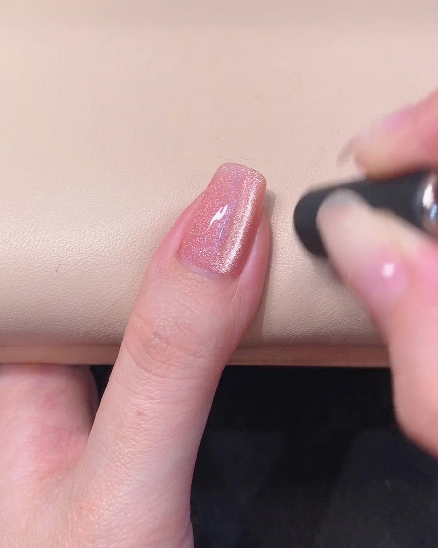 A close-up of a pink gel nail with a glowing magnetic cat-eye stripe visible in the wet gel surface.