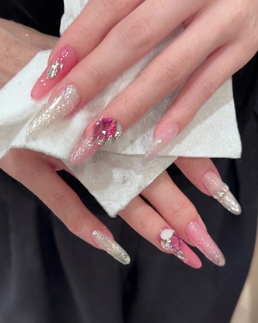 A close-up of long almond-shaped nails showcasing detailed pink and silver glitter reflections.