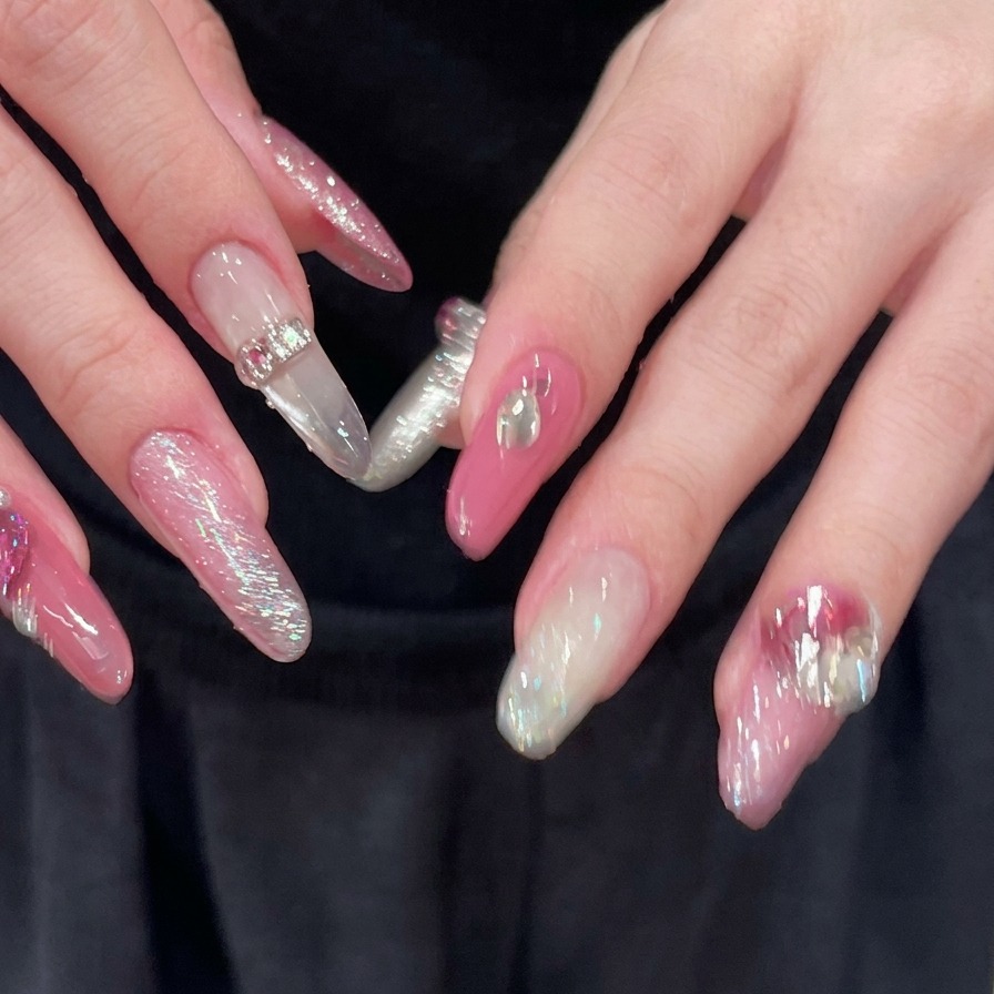 A close-up of hands with fingers spread, revealing fully decorated pink and silver long almond nails with sparkly rhinestone accents.