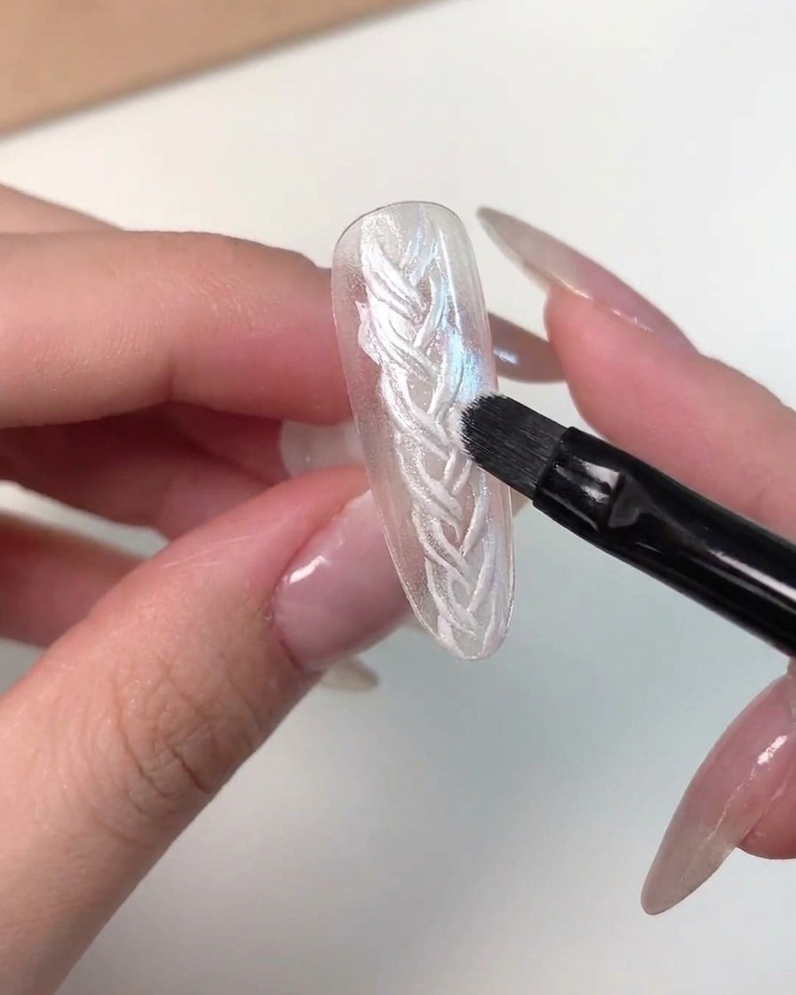 A detailed close-up showing a brush applying pink magnetic cat eye gel onto a nail tip.