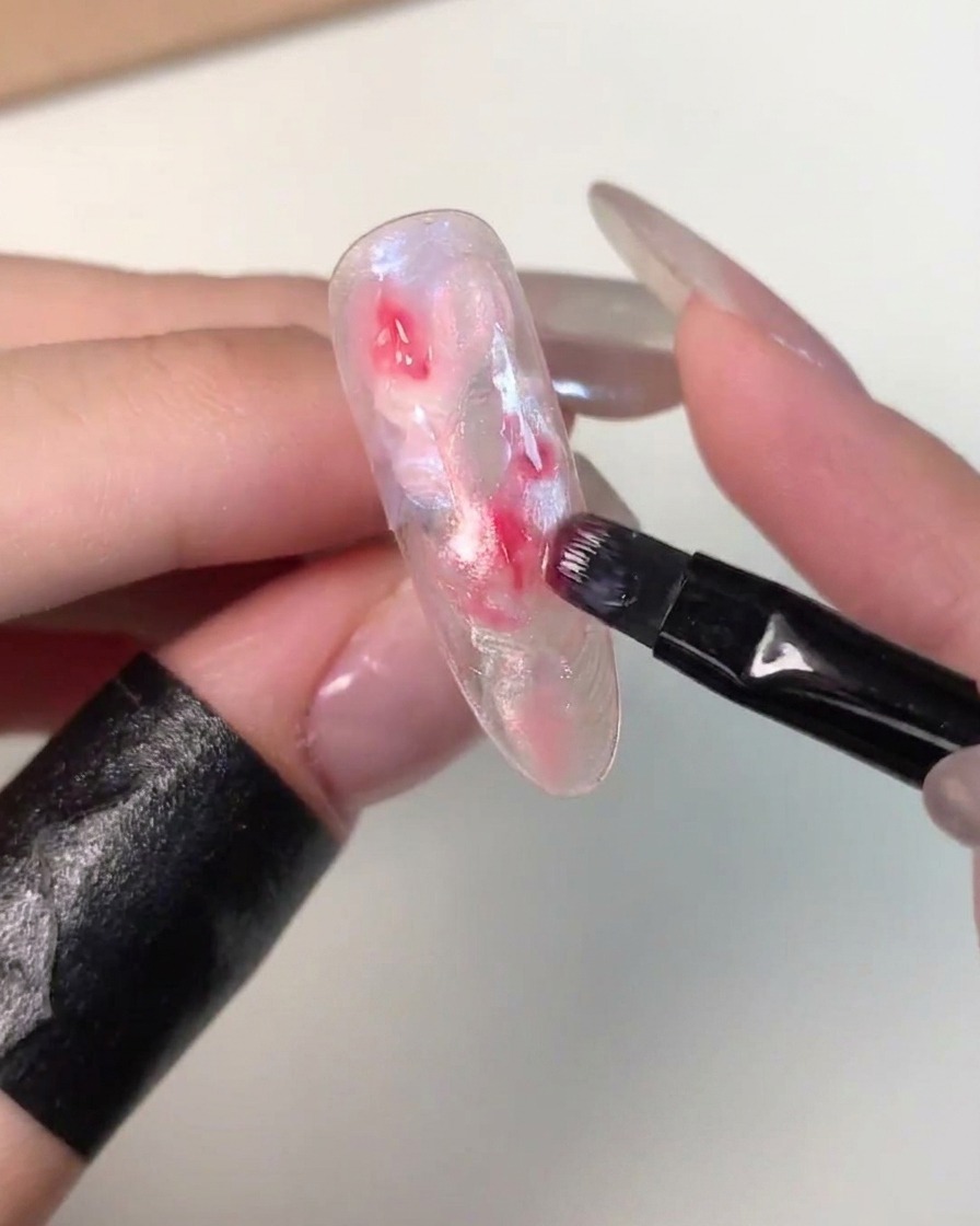 A small flat brush dabbing darker pink gel onto the center of an uncured marbled nail tip.