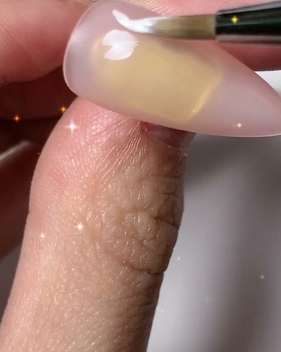 A nail brush adding white petals to complete multiple flower outlines across the nail plate.