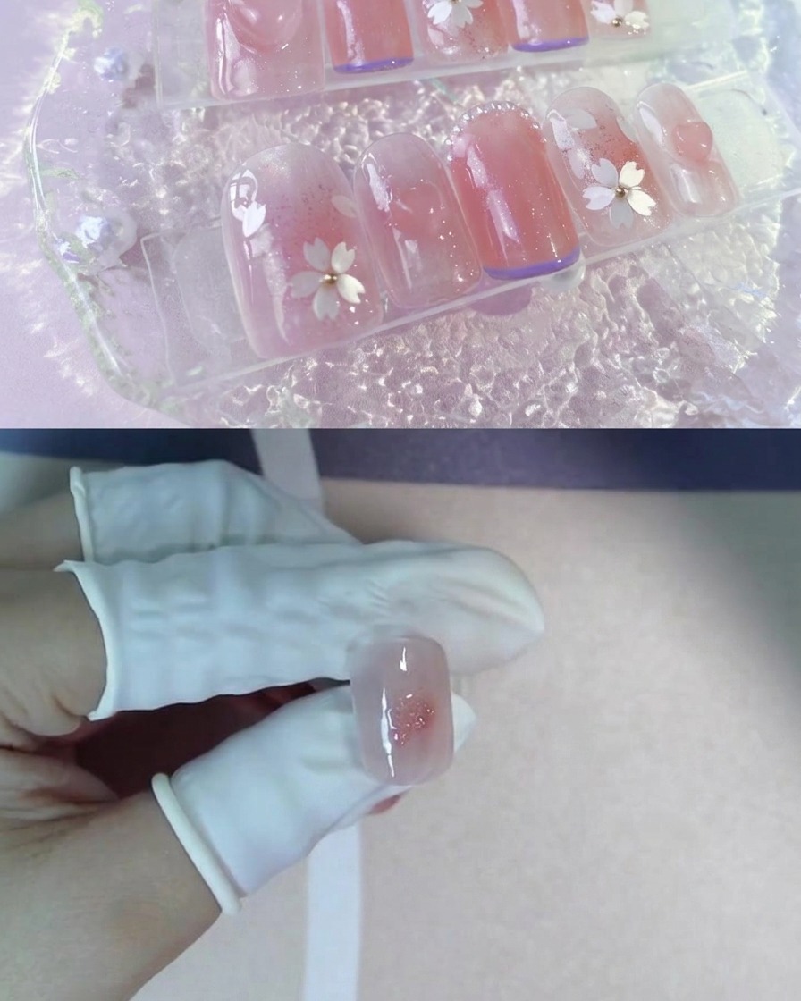 A gloved finger holding a nail tip with a pink blush center and a dot of sparkly gel.