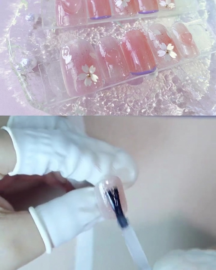 A hand applying a layer of clear reinforcement gel over a blush pink nail.