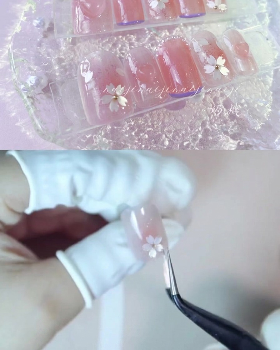 A pair of tweezers carefully placing white cherry blossom petal fragments onto a glossy nail.