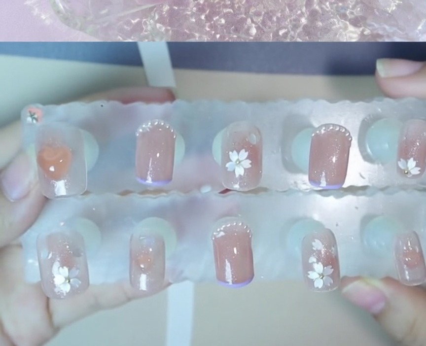 A close-up view of a small steel bead being positioned at the center of a floral nail art design.