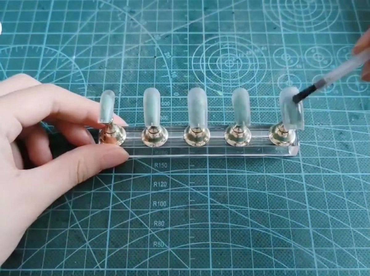 A brush applying a layer of translucent cat-eye gel onto a false nail tip.
