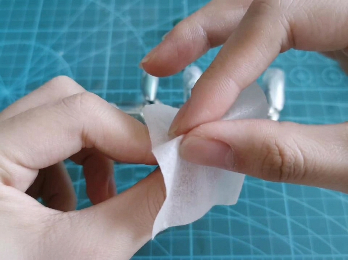 An alcohol wipe cleaning the tacky residue off a cured gel nail tip.