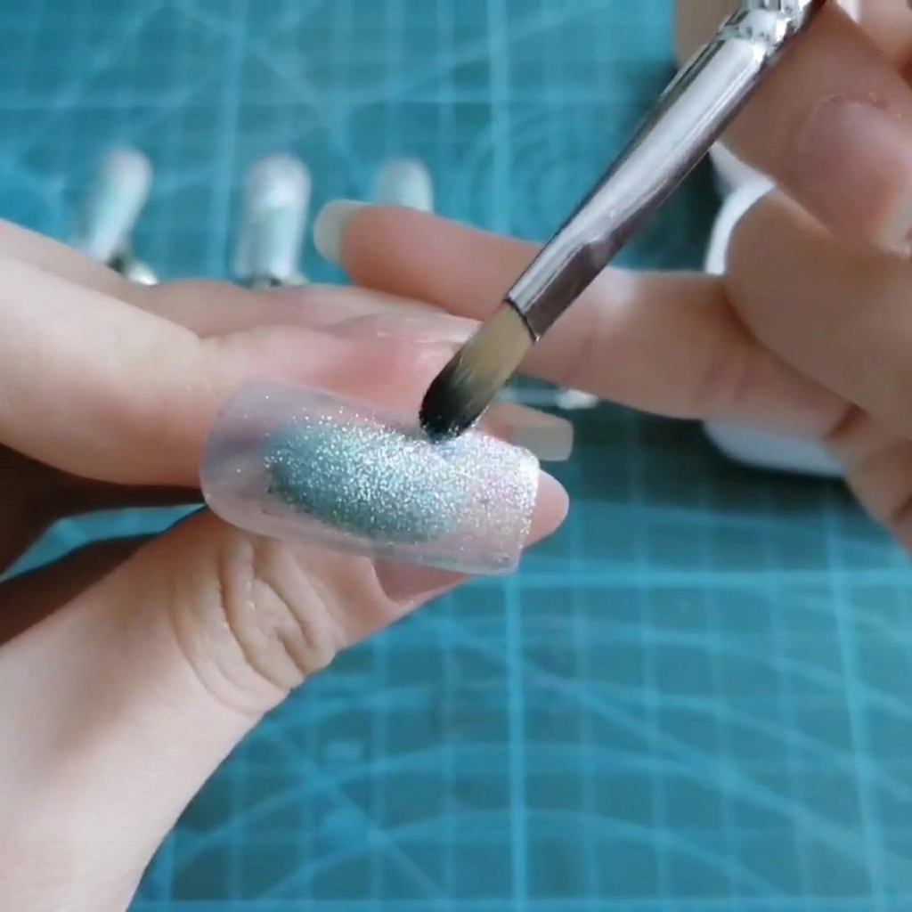 A brush dabbing sheer blue gel onto the middle of a nail tip.