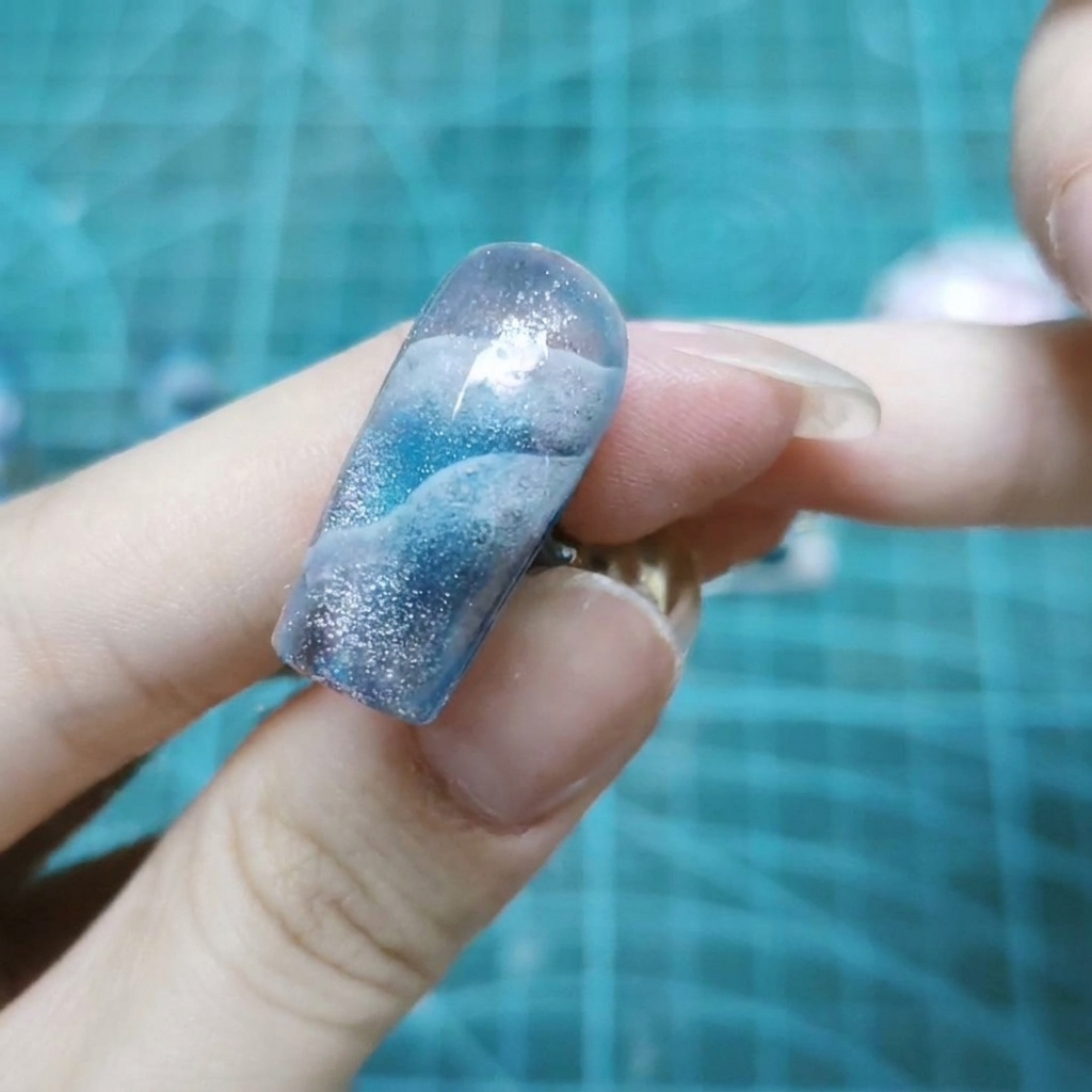 A close-up view of a single nail covered in sparkling holographic glitters embedded in clear gel.