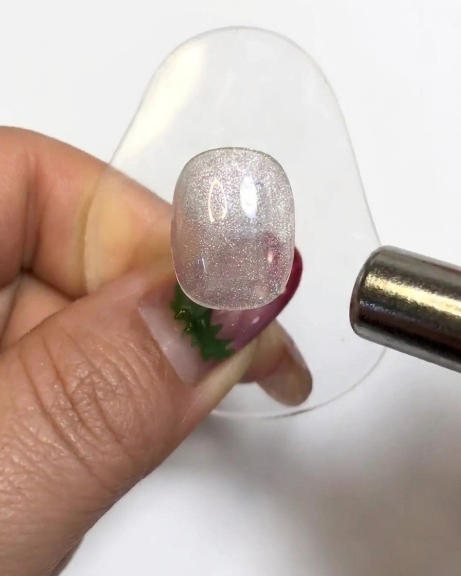 A cylindrical magnet hovering over a sparkly gel nail tip to activate the cat eye particles.