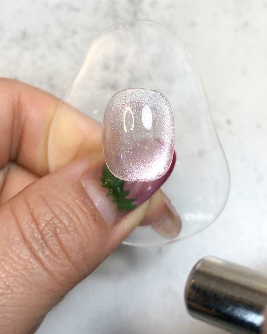 A handheld UV lamp illuminating a sparkly magnetic gel nail on a stand to cure it.