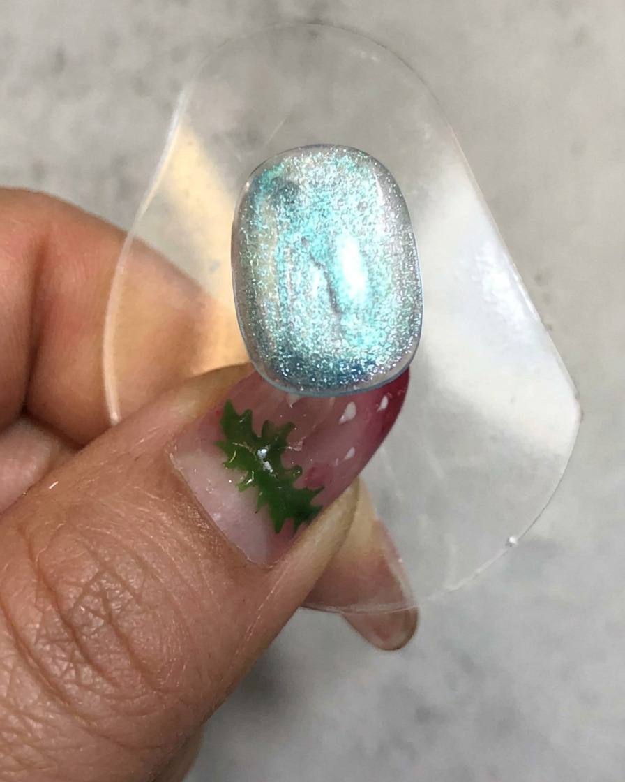 A nail placed inside a curing lamp with a glowing light emitting around the translucent blue gel surface.