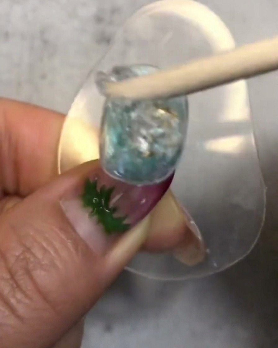 A wooden stick stirring and placing a dollop of translucent soft candy gel onto the decorated nail.