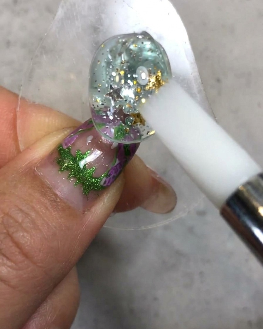 A white silicone pen sculpting and smoothing the soft candy gel texture on top of the decorated nail surface.