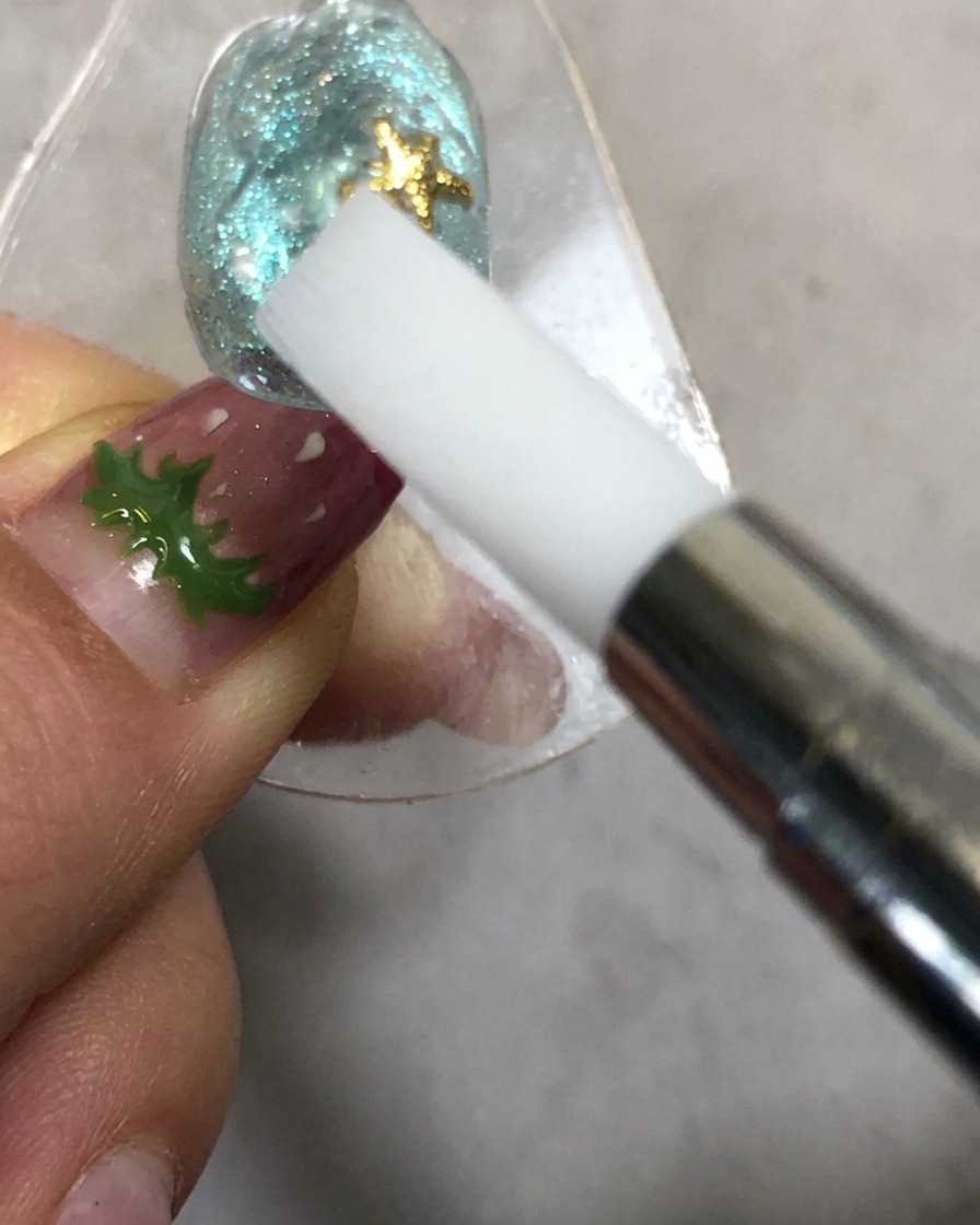 A hand holding a silicone shaping tool near a nail under a curing lamp.