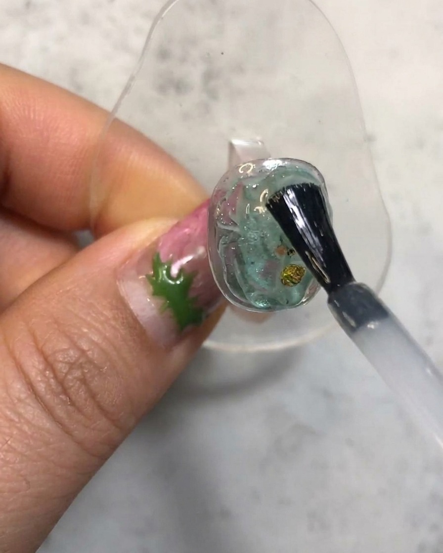 A nail brush applying a clear top coat over a textured translucent gel nail.