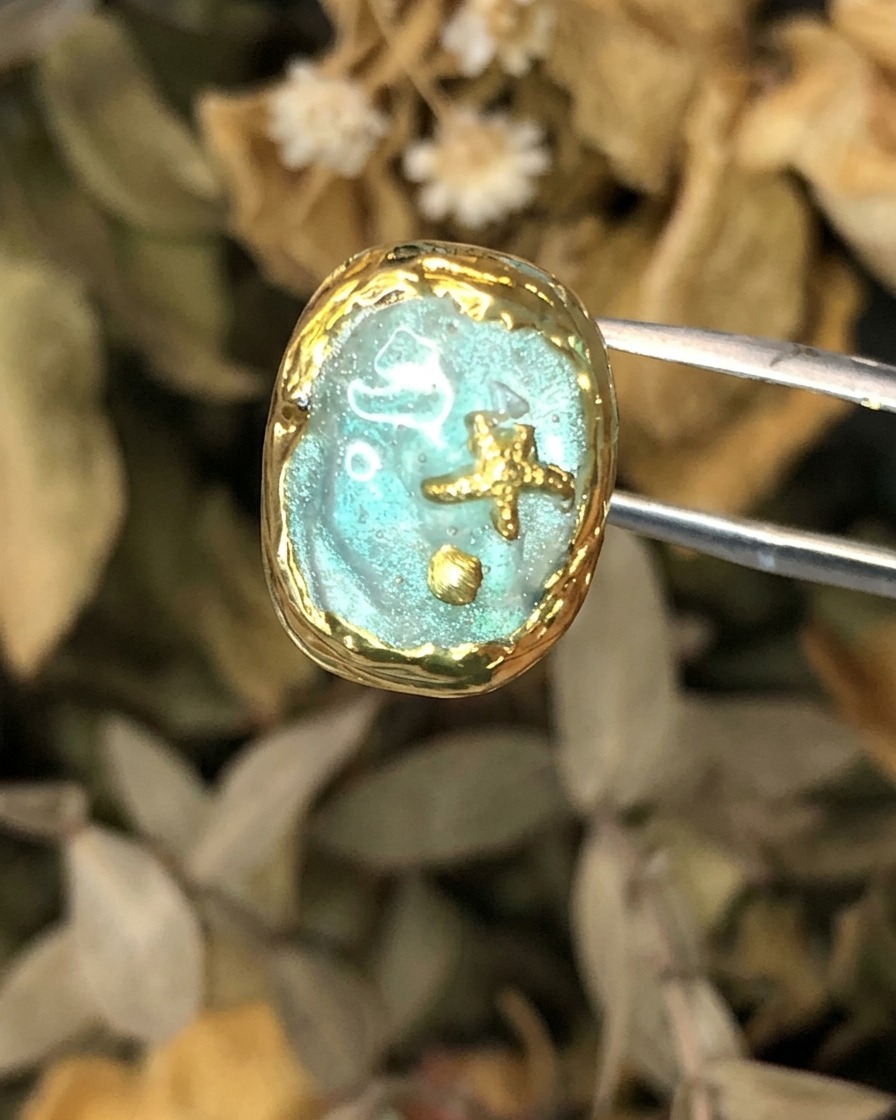 A pair of tweezers holding a completed Atlantis-themed nail art piece with gold framing.