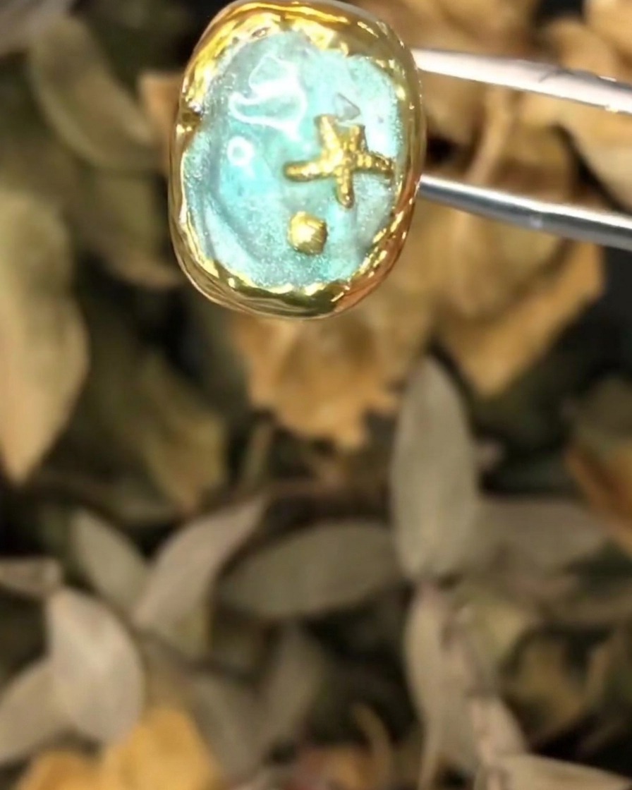 A pair of tweezers holding the textured ocean nail art piece during the final coat application.