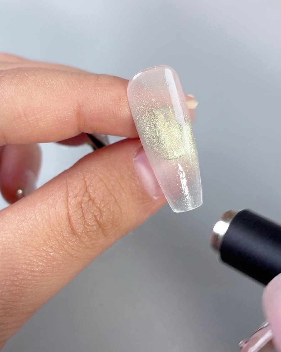 A cylindrical magnetic wand held close to a glossy green gel nail to activate the cat-eye effect.