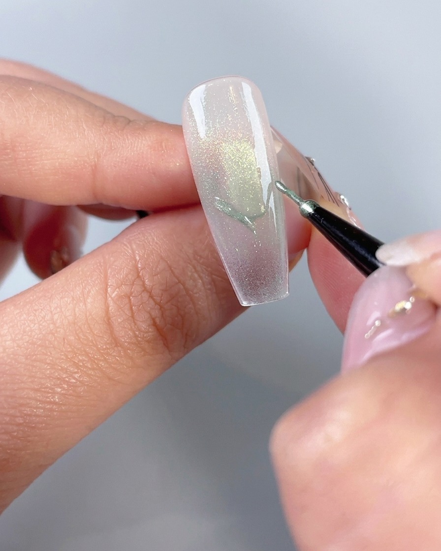 A fine nail art brush drawing butterfly wing outlines on a manicured nail tip.
