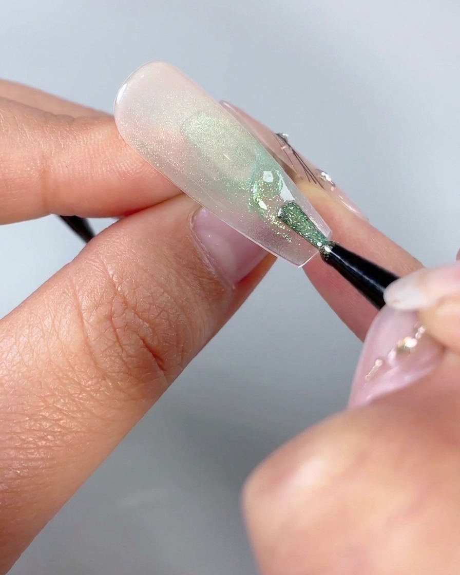 A fine nail art brush drawing small curved triangle shapes near the lower base of a butterfly nail design.