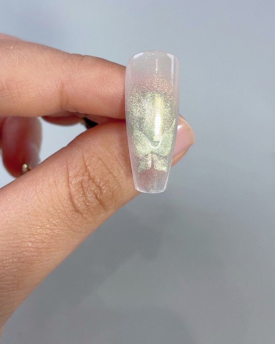 A close-up of a clear nail tip displaying glowing green cat-eye butterfly wing shapes after magnetic activation.