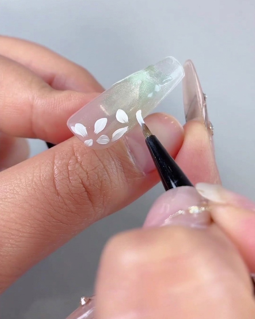 A fine art brush adding smaller white petal details around the previously painted large floral base.