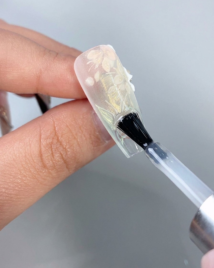 A nail brush applying a clear top coat to the underside of a clear extension nail tips free edge.