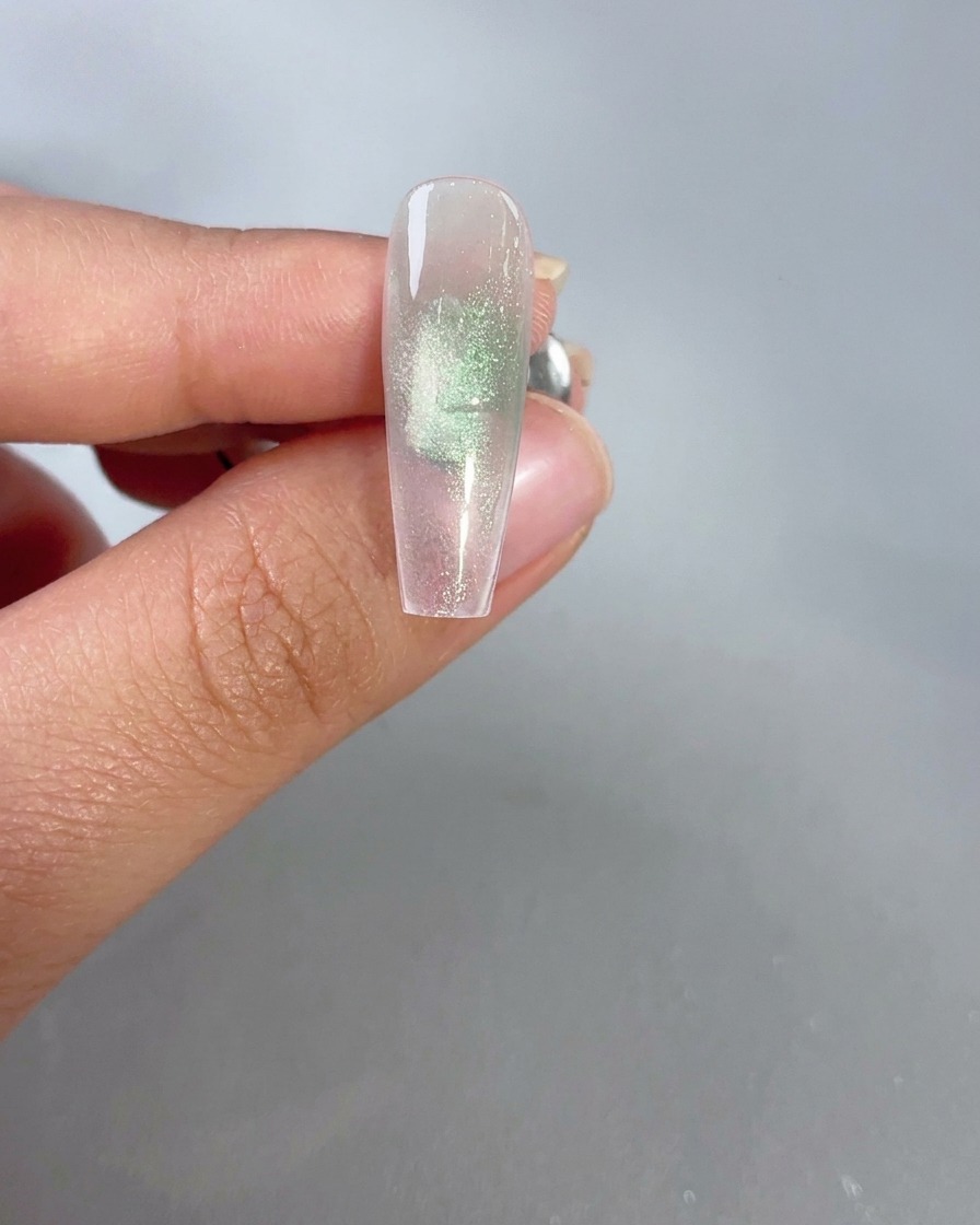 A magnet held close to a sheer green cat-eye gel nail to activate the shimmer effect.