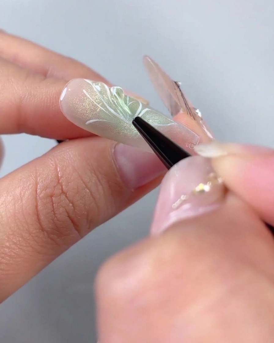 A fine liner brush applying clear 3D modeling gel over the white painted wing outlines of a half-butterfly nail design.