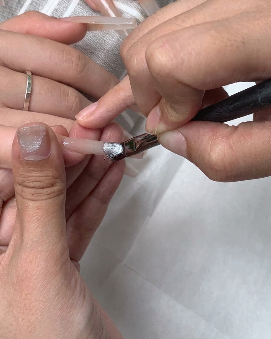 A flat gel brush applying silver cat-eye gel across the entire nail.