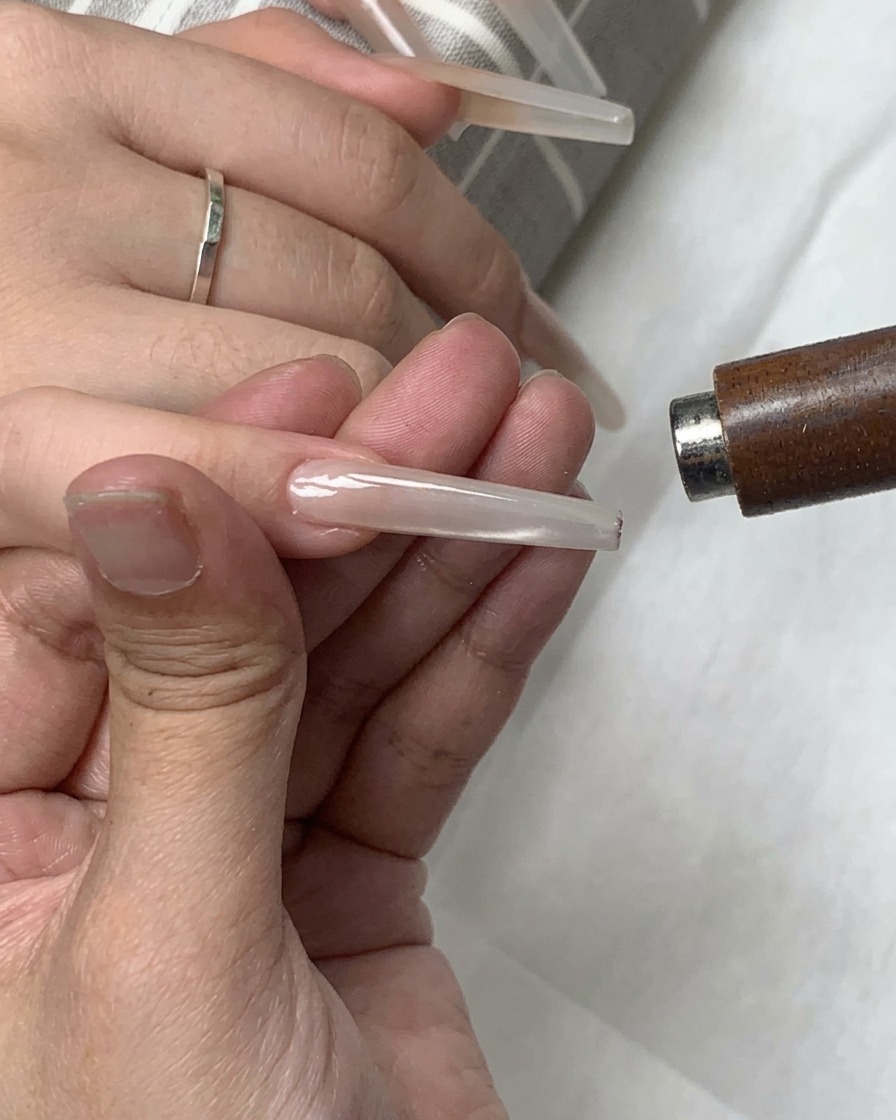 A cylindrical magnet being used to shape magnetic particles into a glowing light band on the nail.