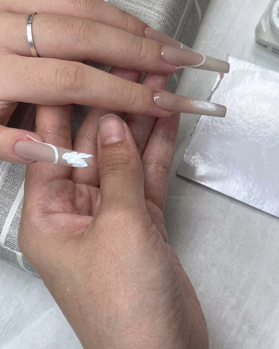 A French tip guide sticker placed on the nail while white gel polish fills the tip area.