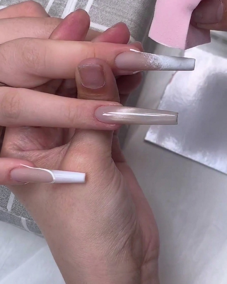 A pink makeup sponge dabbing white gel polish on the tip of a long coffin-shaped nail to create a gradient effect.