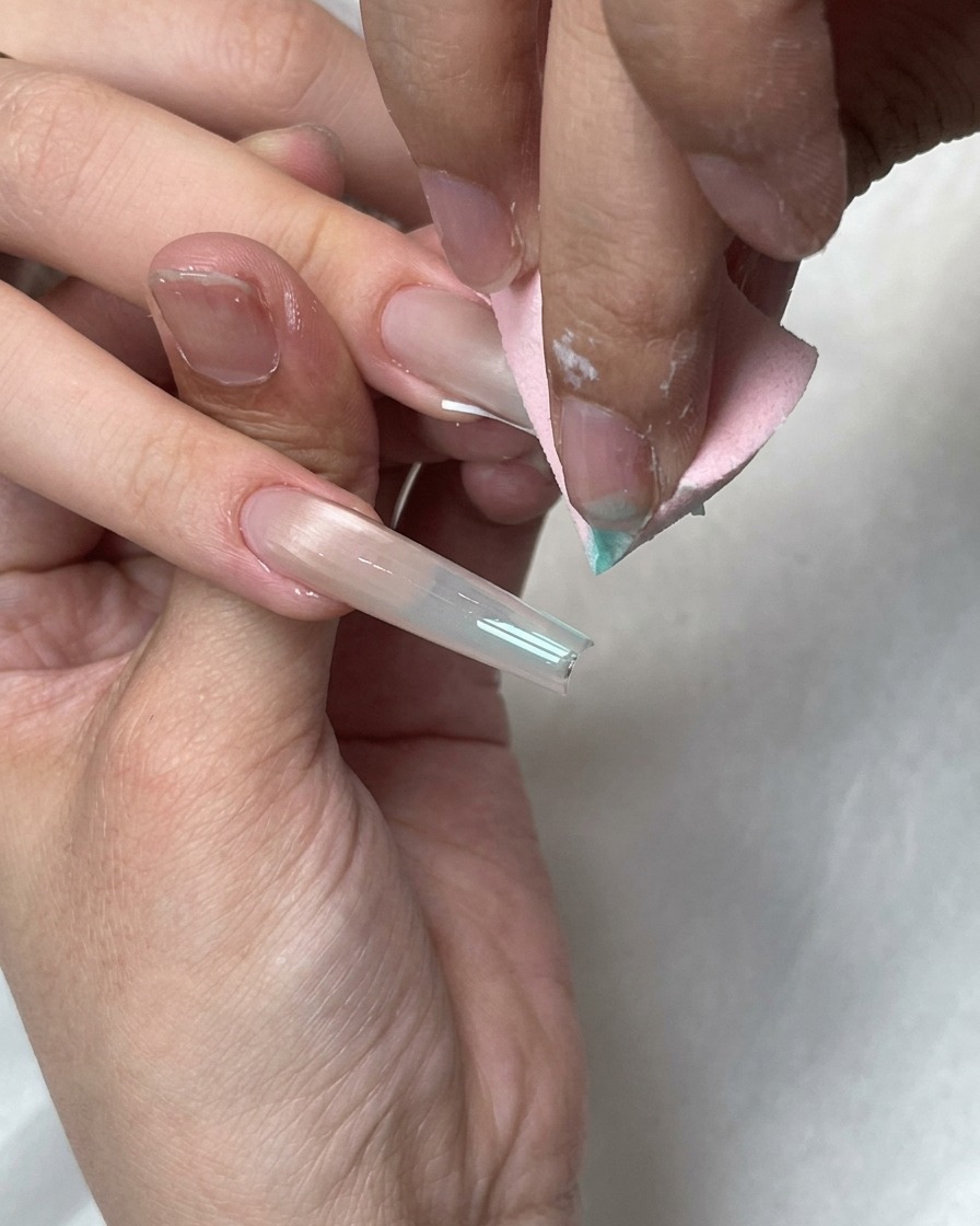 A pink makeup sponge blending blue gel dots onto the white French tip of a long nail.