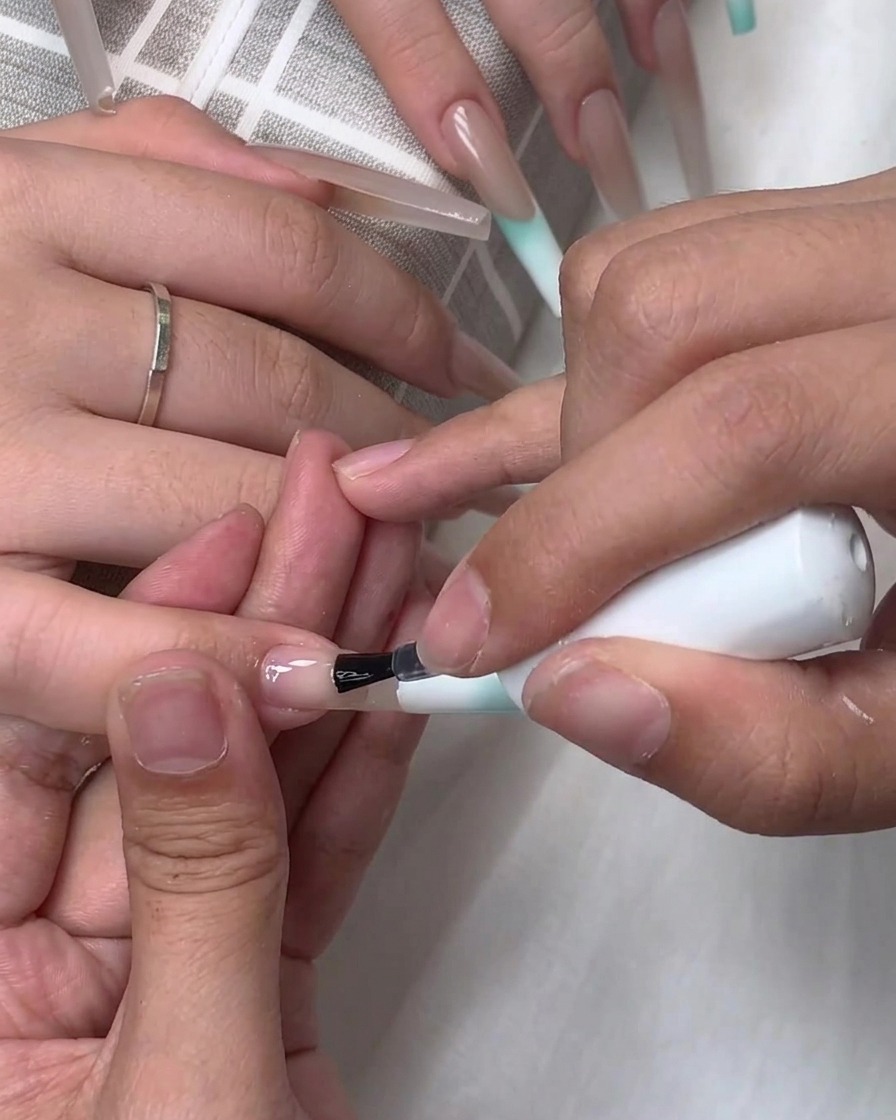 A brush applying clear base or top coat onto the surface of an extended nail.