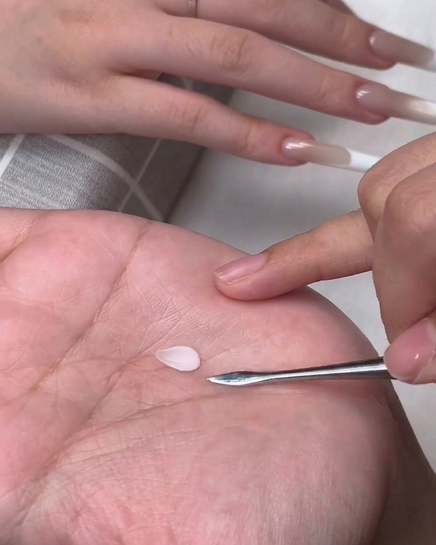 A small teardrop-shaped white 3D gel petal resting on a persons palm next to a metal carving tool.