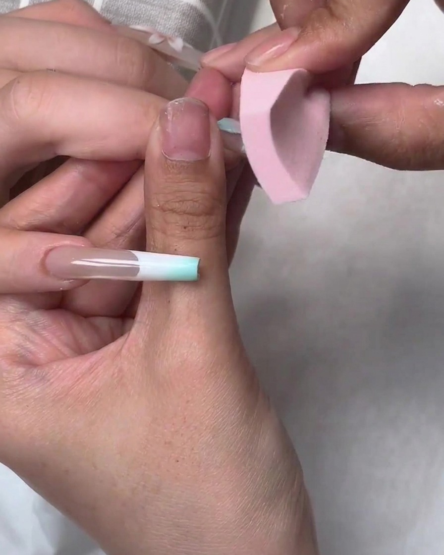 A small pink sponge dabbing blue gel polish onto the edges of a nail application during a nail art tutorial.