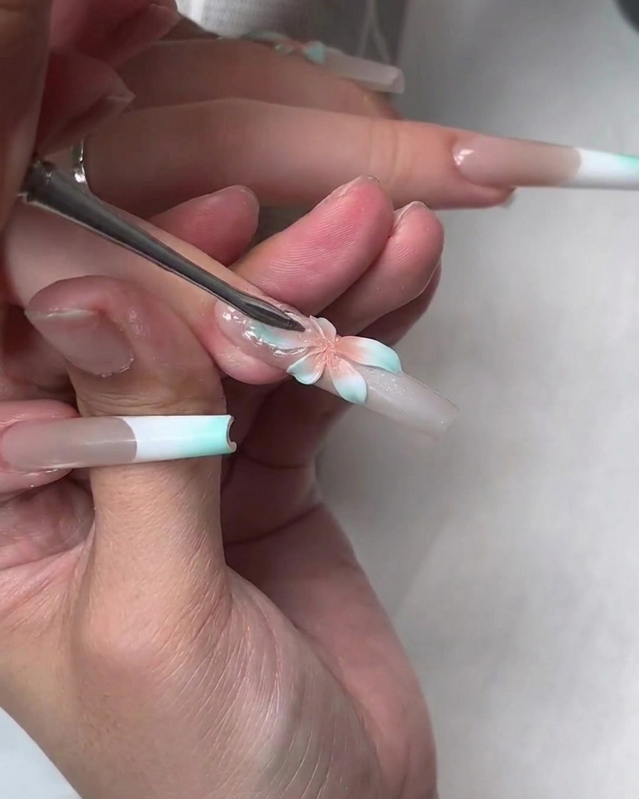 A tool pressing a clear soft builder gel layer over the painted flower to create larger translucent petals.