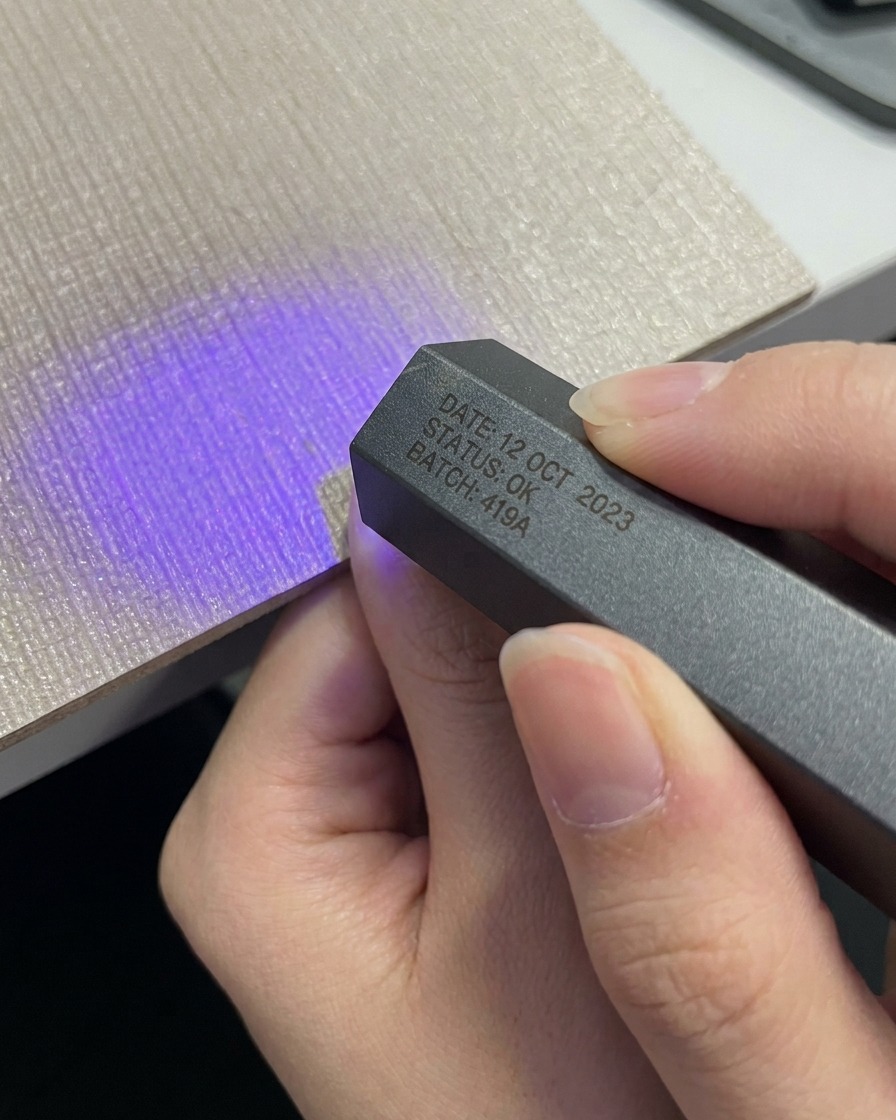 A hand placing a thumb under a compact grey portable UV LED lamp.
