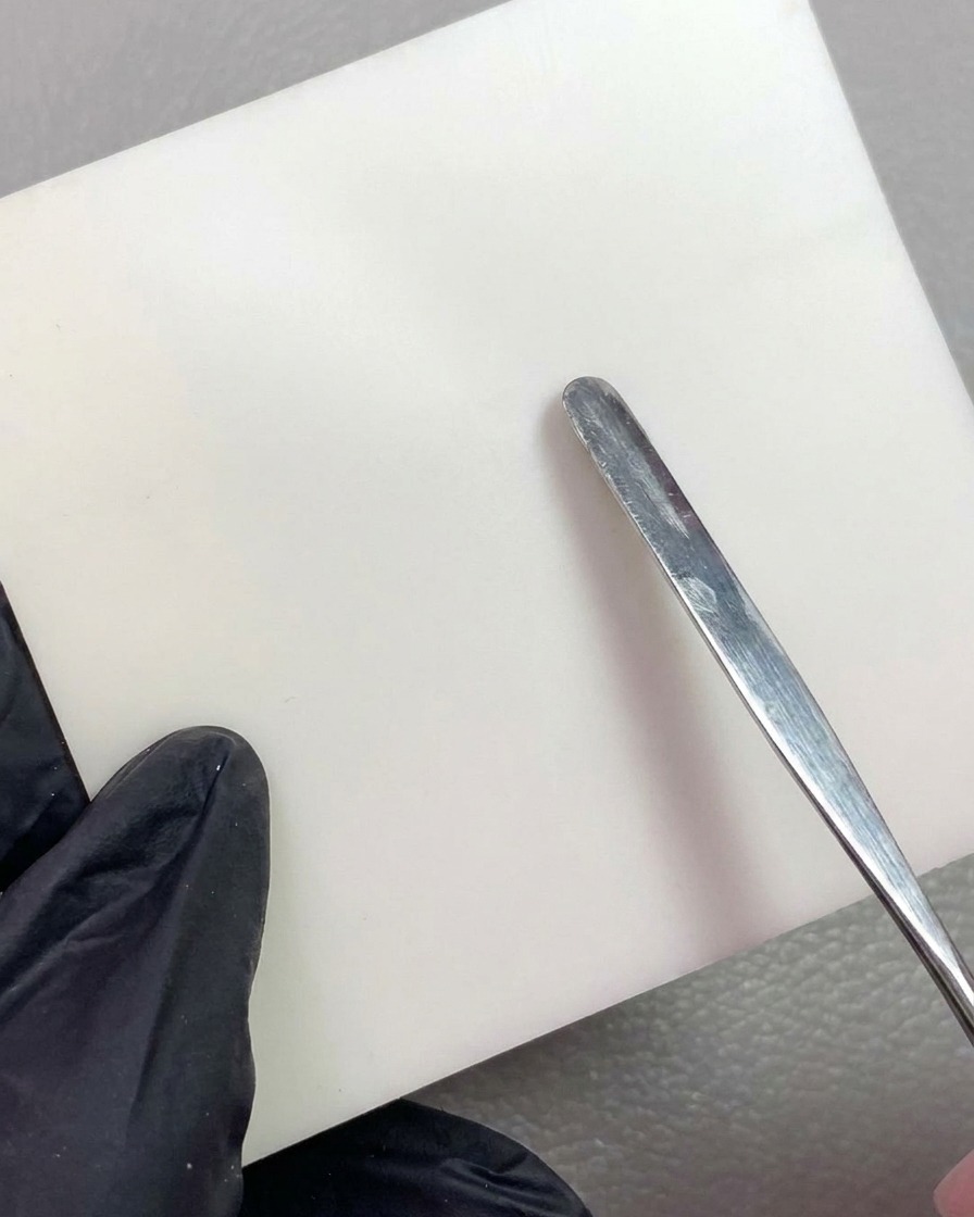 A metal tool placing a piece of white carving gel onto a clean white mixing palette.