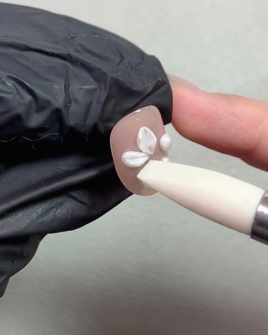 A silicone pen tool pressing and shaping white pearl gel balls into flower petals on a nude painted nail.