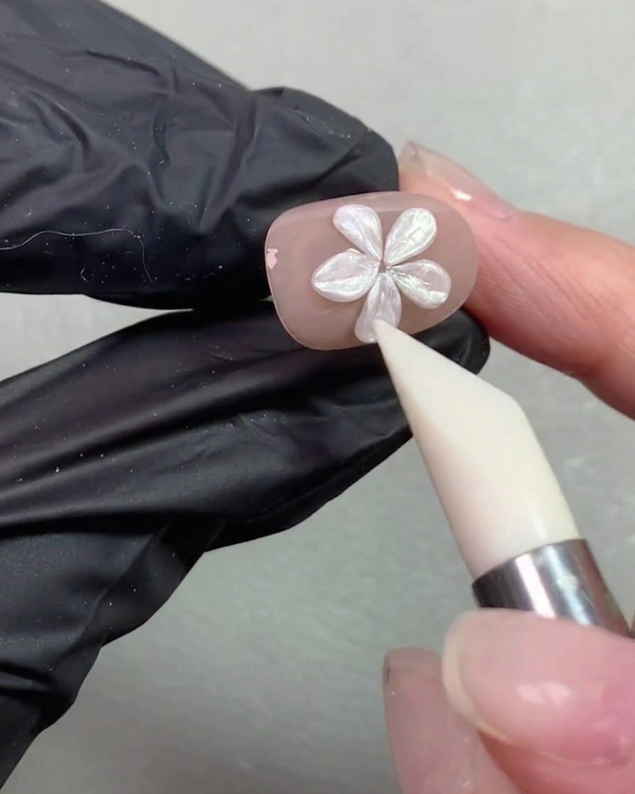 A silicone shaping pen smoothing and adjusting the petal shape of a pearl flower on a nude-colored nail.
