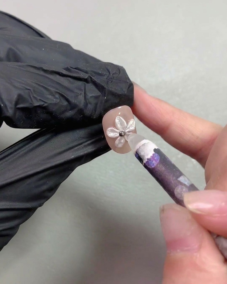 A wax picker tool placing tiny metallic steel beads into the center of a pearl flower nail art.