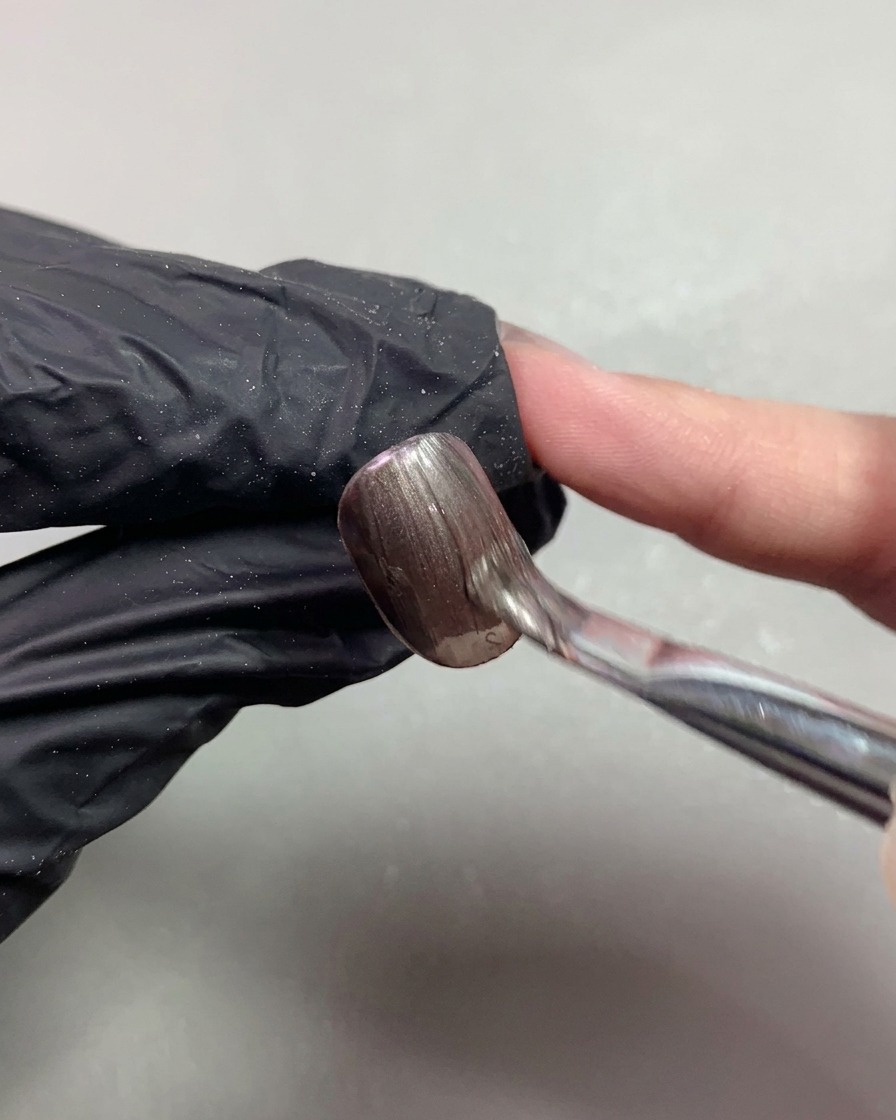 A brush applying dark brown magnetic cat-eye gel smoothly onto a short nail.