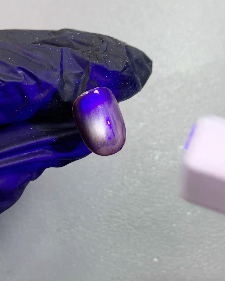 A close-up view of a dark brown magnetic cat-eye nail being cured under a small UV lamp.